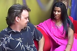 Young Indian lady gives an older man a blow job on a red couch poster
